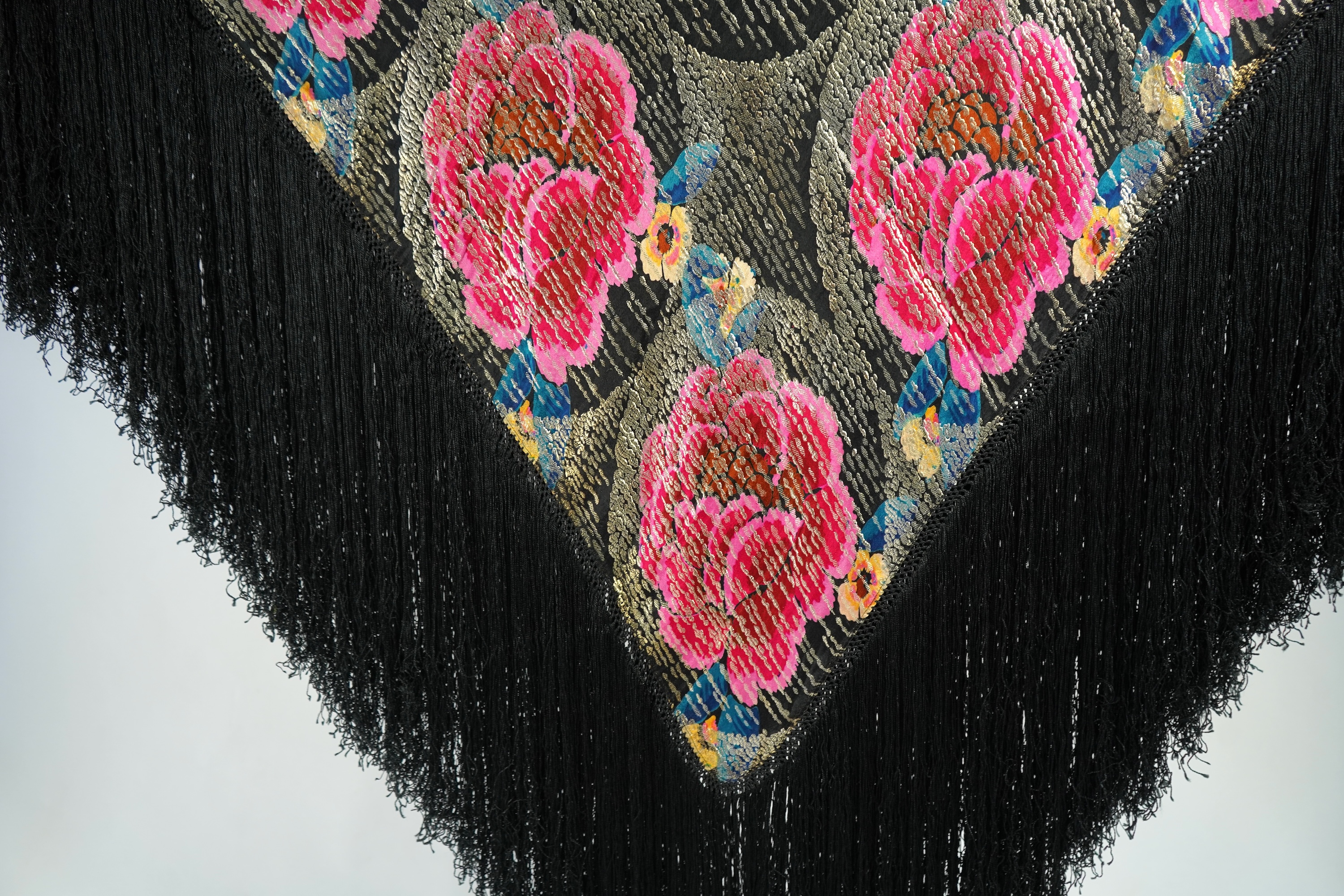 A 1930's ‘jazz age’ black and coloured silk lame evening shawl. Woven with giant pink and red roses and silver thread stripes, edged with long silk fringing. 118cm x 123cm. Condition - colours and silk strong. Fringing g